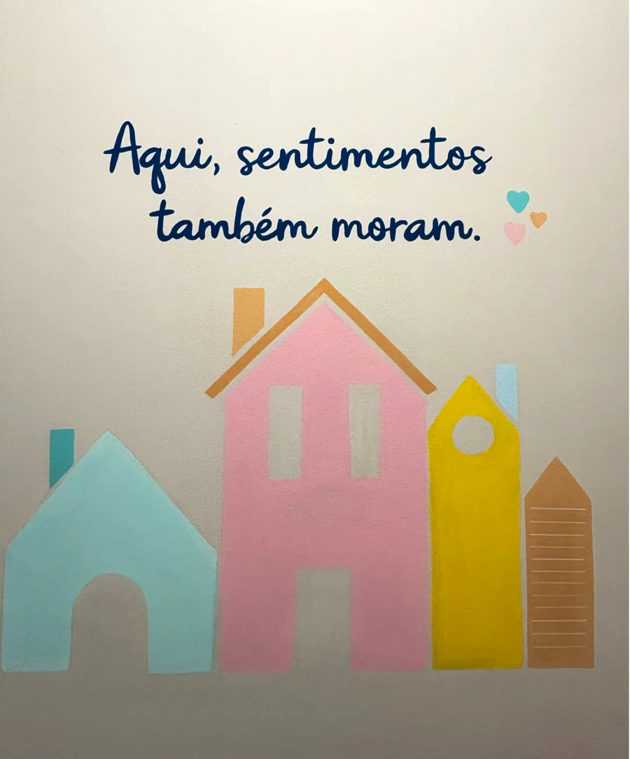 Parede com casinhas coloridas recortadas e a frase Aqui, sentimentos também moram
