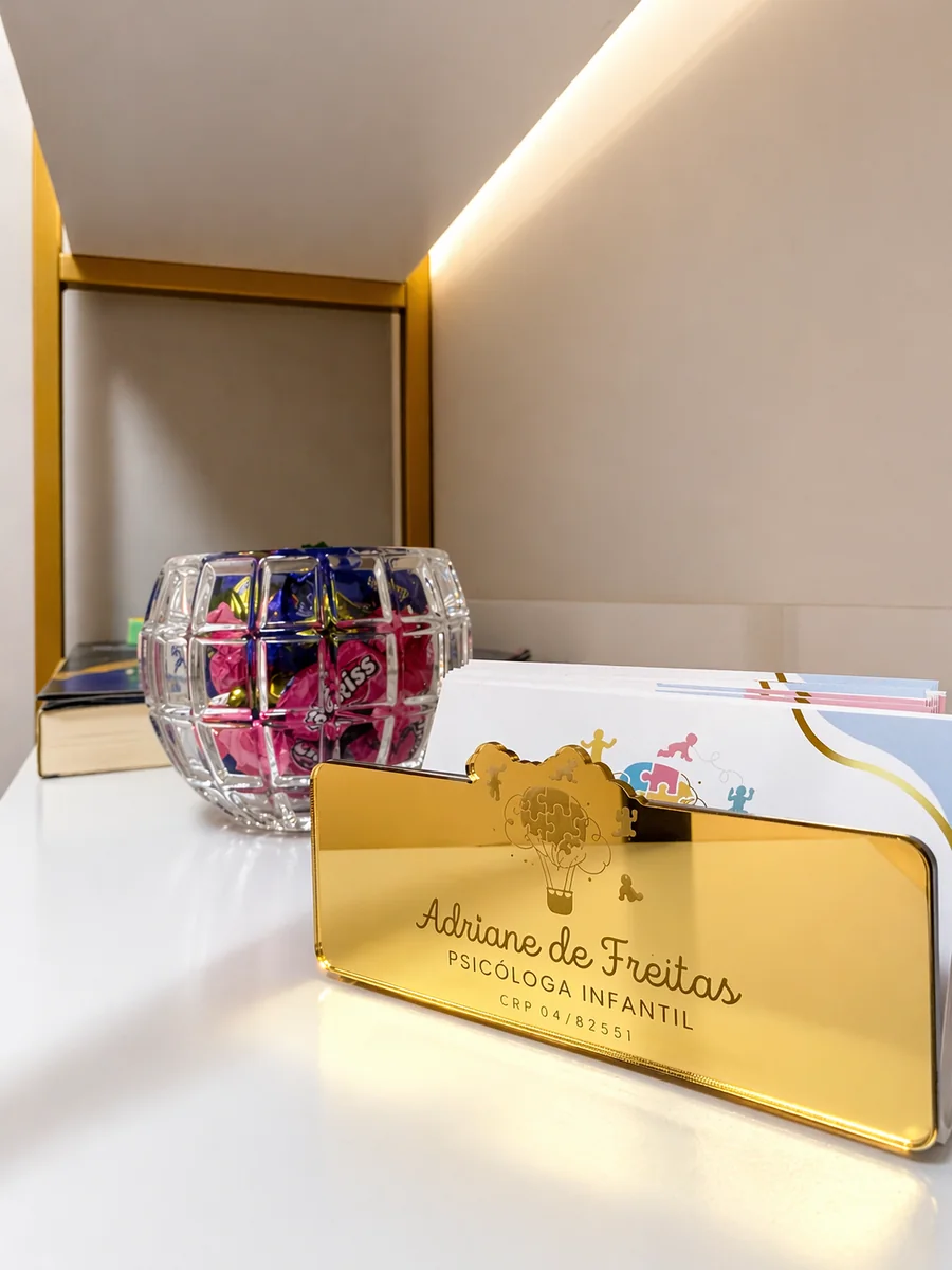 Placa dourada com o nome Adriane de Freitas, psicóloga infantil, sobre a mesa